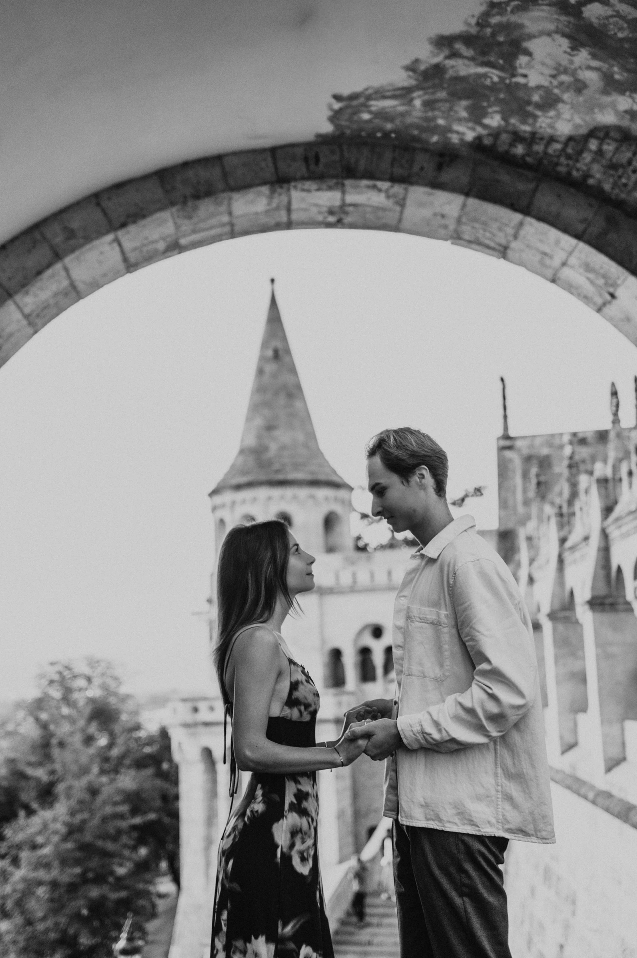 Black-and-white portrait of the couple holding hands beneath an arch during their Budapest photoshoot at Fisherman’s Bastion.