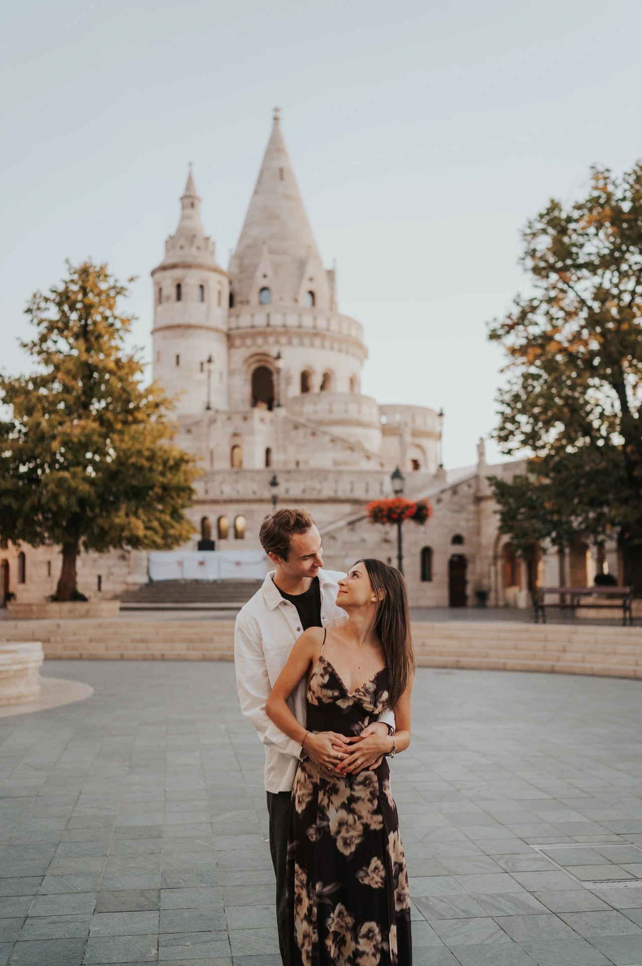 The man embracing his partner from behind in front of Fisherman’s Bastion during their sunny October photoshoot in Budapest.