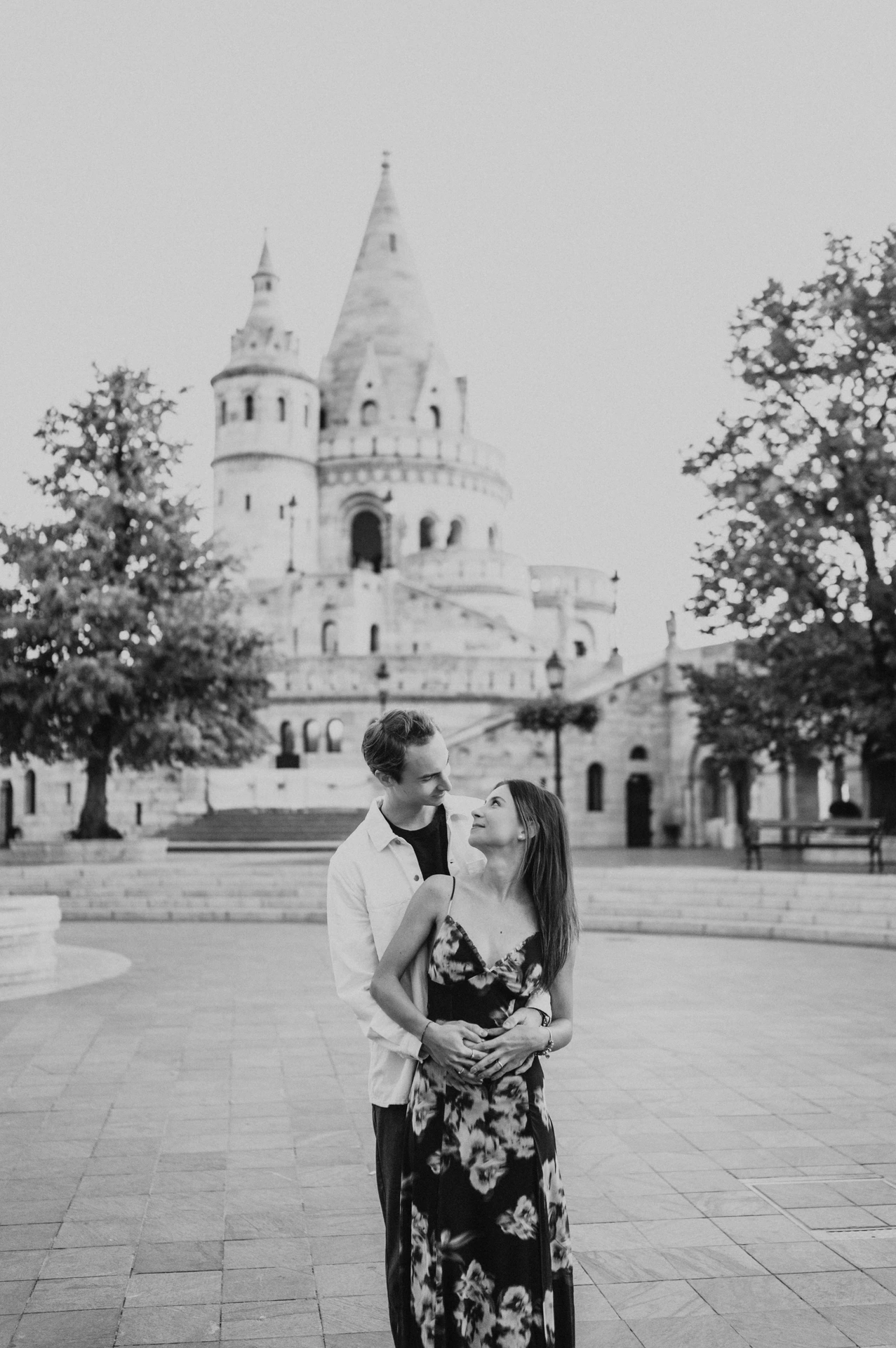 Black-and-white portrait of the couple embracing in the square during their Budapest photoshoot, with pointed towers behind them.