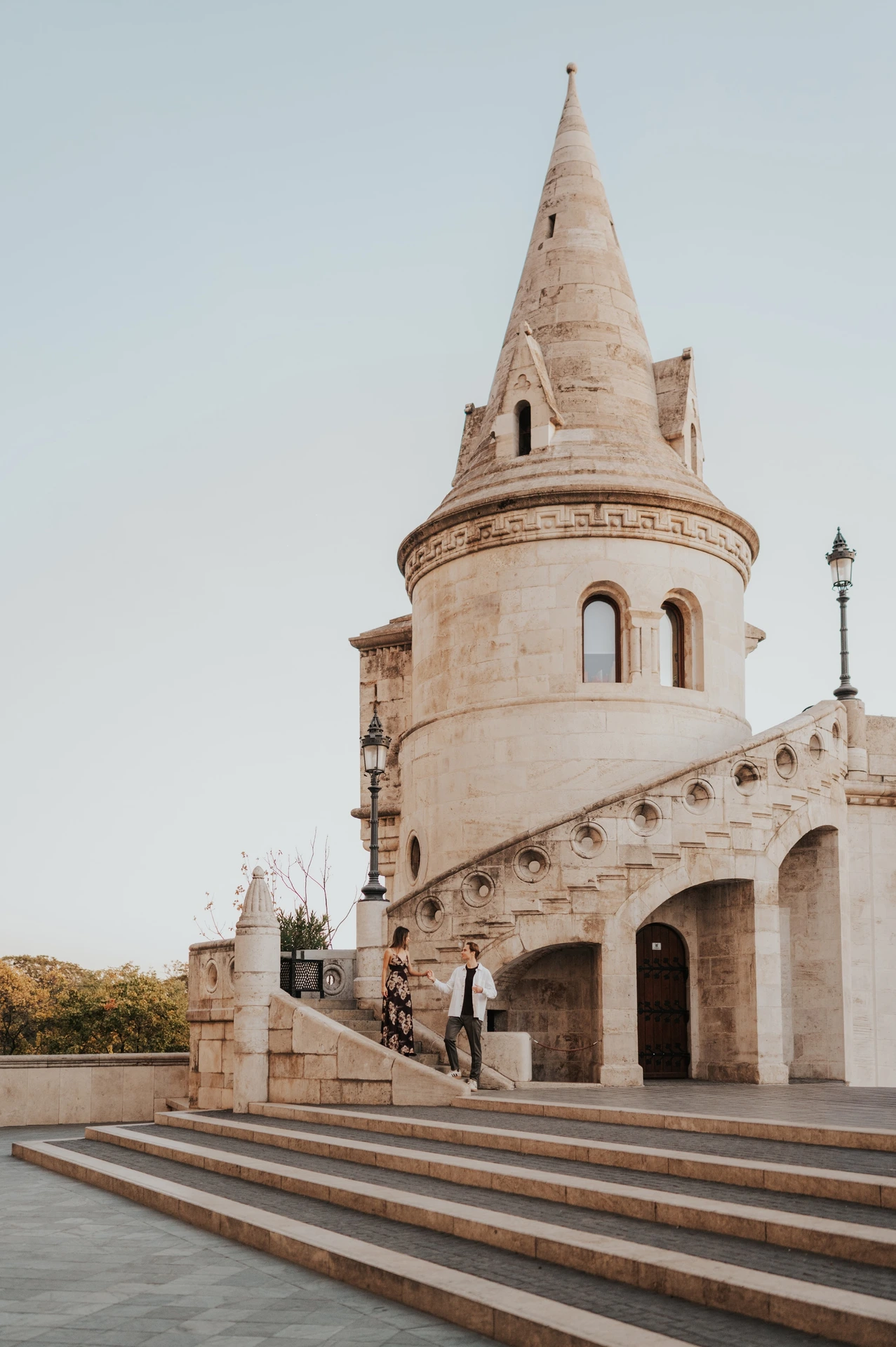 Wide architectural view of the couple on the steps below a tall turret during their Budapest photoshoot at Fisherman’s Bastion.