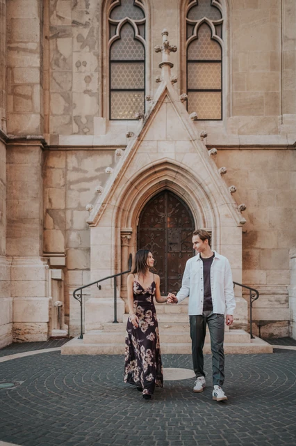 Photoshoot in Budapest walking from the carved church doorway The couple walking hand in hand away from the carved church doorway during their Budapest photoshoot.