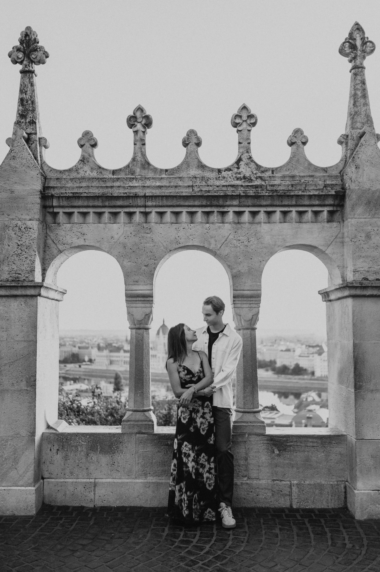 Black-and-white portrait of the couple embracing beside the open terrace arches during their Budapest photoshoot at Fisherman’s Bastion.