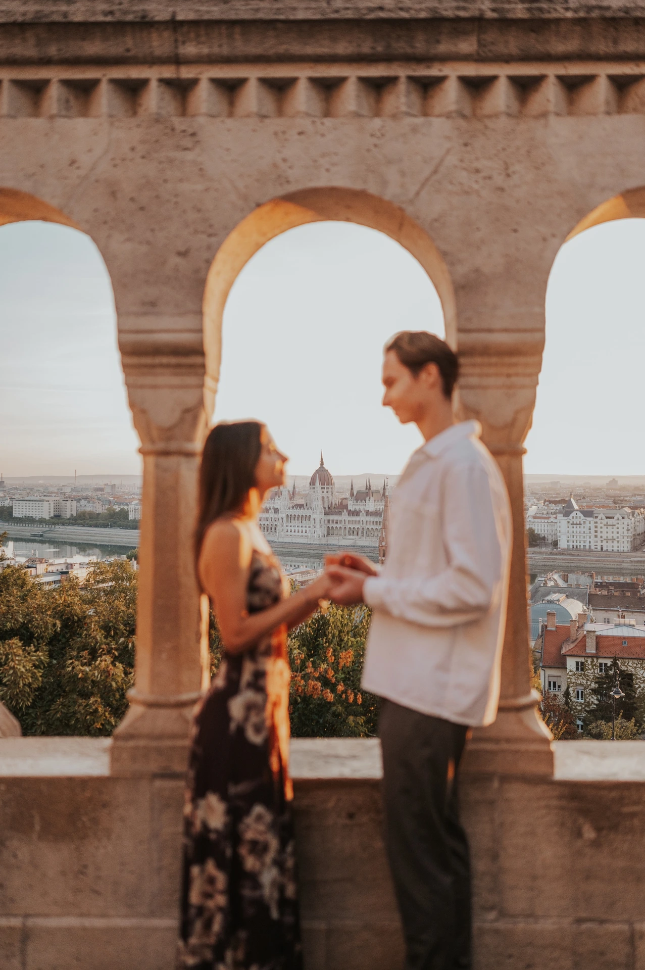 A closer portrait of the couple holding hands beside a sunlit stone arch during their Budapest photoshoot at Fisherman’s Bastion.