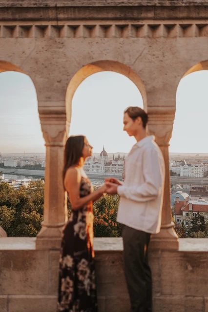 Sunlit couple photoshoot in Budapest beside a stone arch A closer portrait of the couple holding hands beside a sunlit stone arch during their Budapest photoshoot at Fisherman’s Bastion.