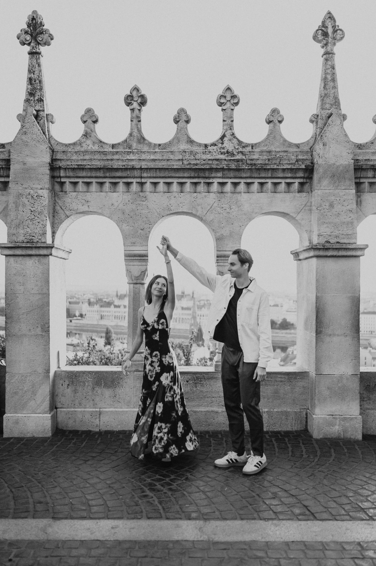 Black-and-white photograph of the couple twirling beneath the terrace arches during their Budapest photoshoot at Fisherman’s Bastion.