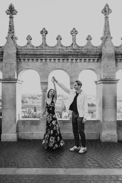 Budapest couple photoshoot with a terrace twirl in black and white Black-and-white photograph of the couple twirling beneath the terrace arches during their Budapest photoshoot at Fisherman’s Bastion.