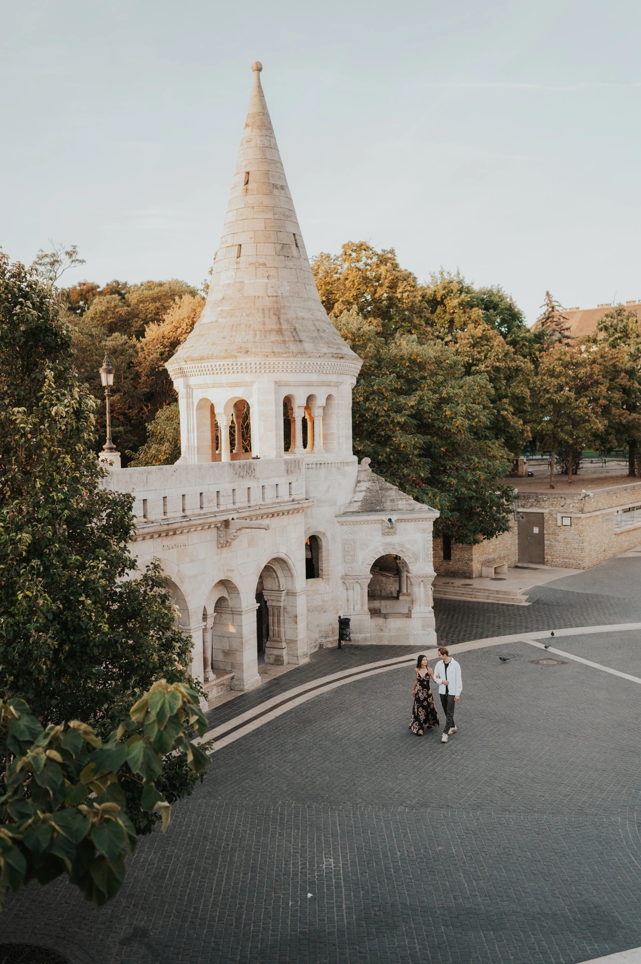 High viewpoint over the couple on the curved walkway beside a pointed turret during their Budapest photoshoot at Fisherman’s Bastion.