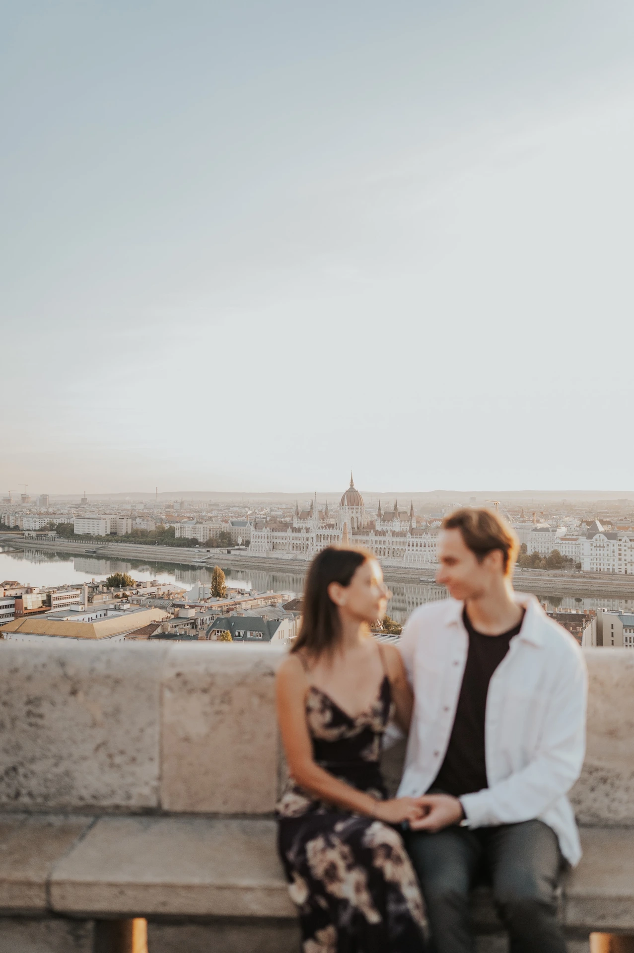 A closer view of the couple seated on the stone bench and holding hands during their Budapest photoshoot above the city.