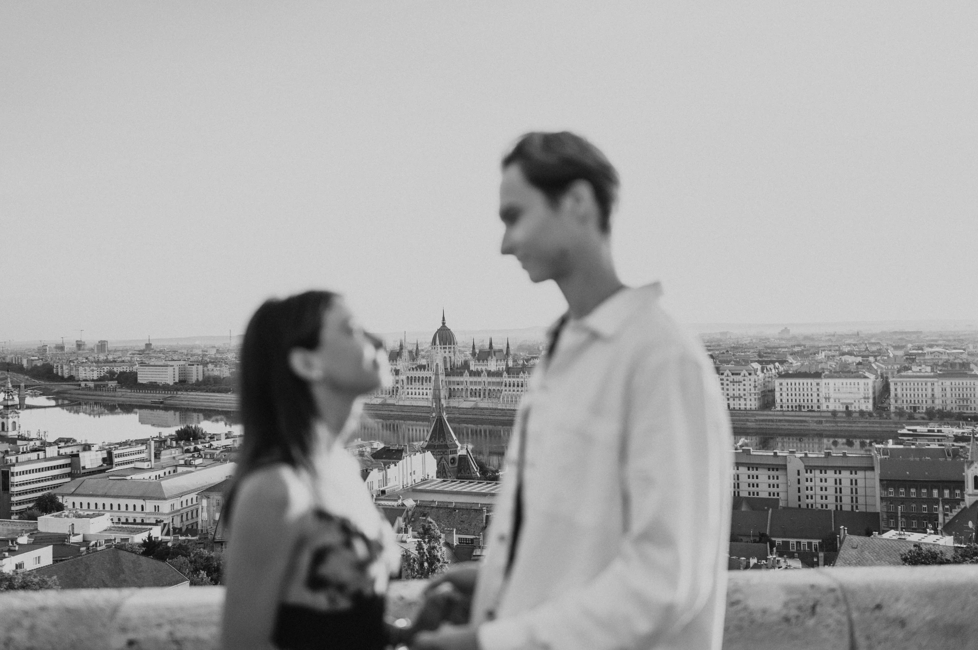 Black-and-white soft-focus portrait of the couple during their Budapest photoshoot, with Parliament and city rooftops behind them.