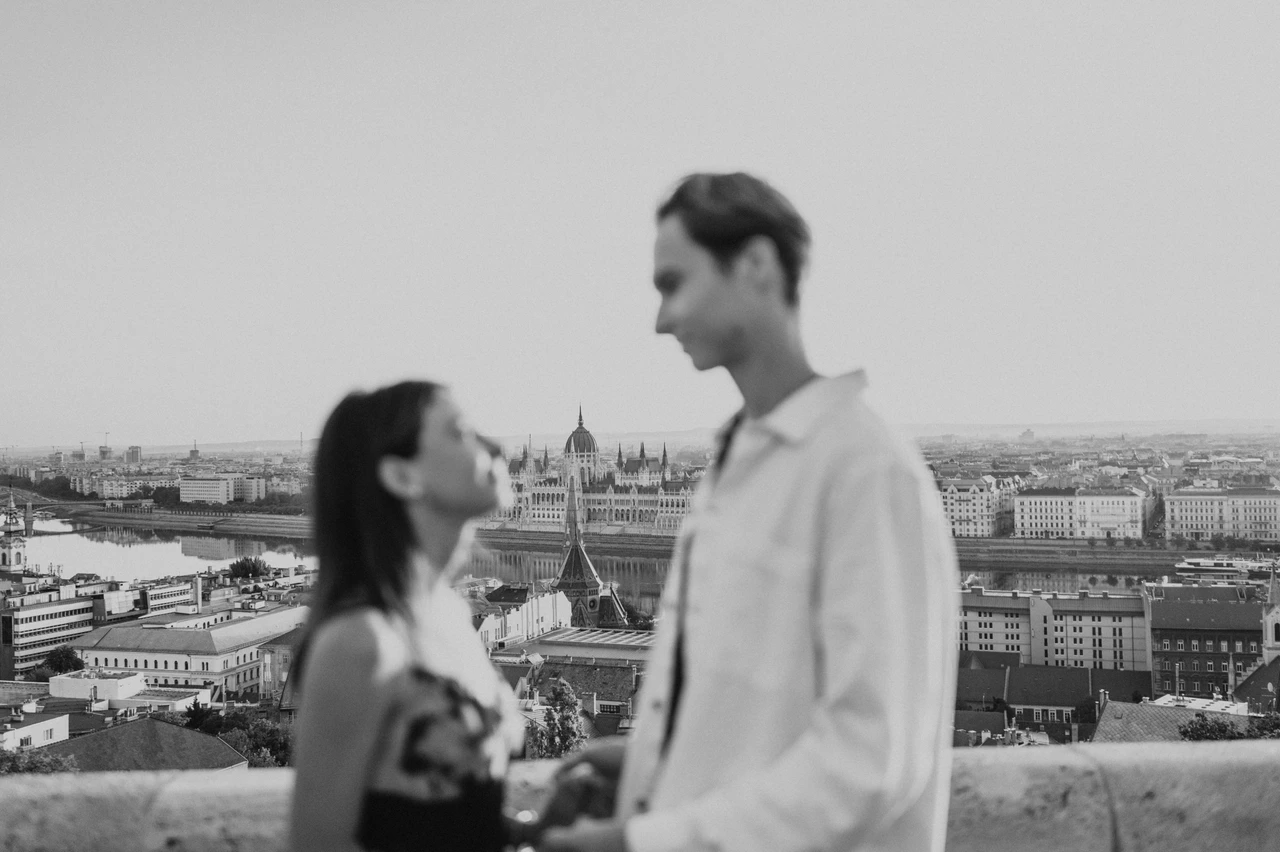 Black-and-white Budapest photoshoot with Parliament in the backdrop Black-and-white soft-focus portrait of the couple during their Budapest photoshoot, with Parliament and city rooftops behind them.