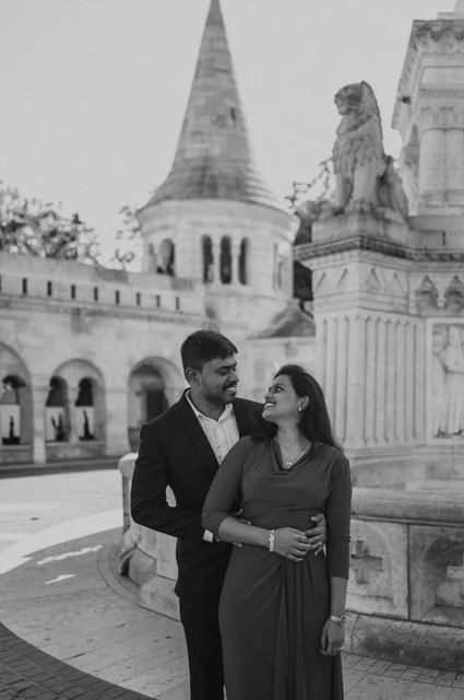 Budapest photoshoot beside the turret in black and white Black-and-white portrait of the couple smiling at one another beside the carved stone monument and a Fisherman’s Bastion turret during their Budapest photoshoot.