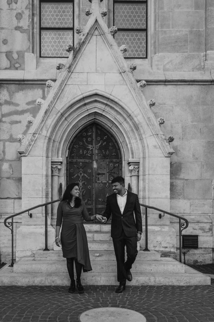 A Budapest photoshoot walk by the church in black and white Black-and-white photograph of the couple walking together in front of the church doorway and curved handrails during their Budapest photoshoot.