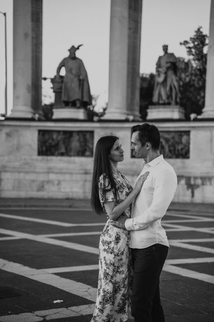 A close embrace in black and white at a Budapest couple photoshoot Black-and-white close portrait of the couple embracing at Heroes’ Square with bronze statues behind them during their couple photoshoot in Budapest.