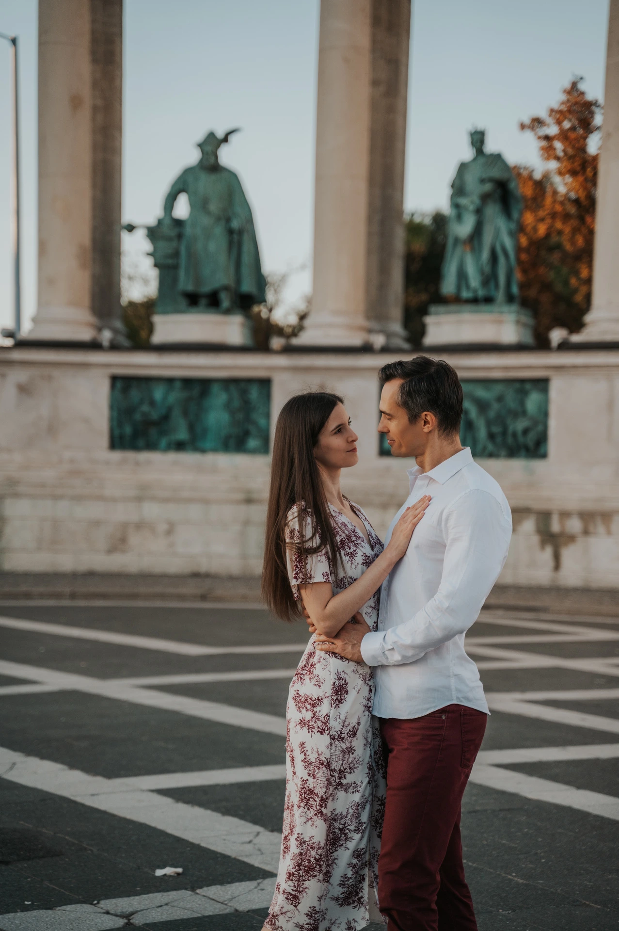 A close portrait of the couple looking at one another with the bronze statues at Heroes’ Square behind them during their couple photoshoot in Budapest.