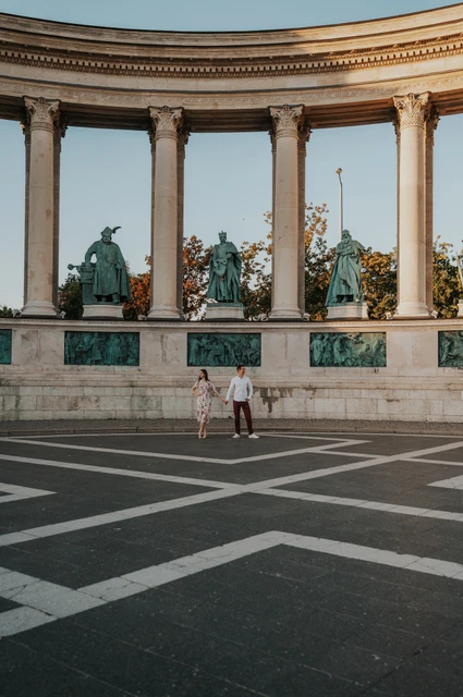 The grand colonnade of Heroes’ Square at a Budapest couple photoshoot The couple standing beneath the curved colonnade and bronze statues at Heroes’ Square during their couple photoshoot in Budapest.