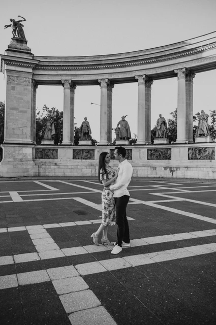An embrace at Heroes’ Square in black and white at a Budapest couple photoshoot Black-and-white portrait of the couple embracing beneath the curved colonnade at Heroes’ Square during their couple photoshoot in Budapest.