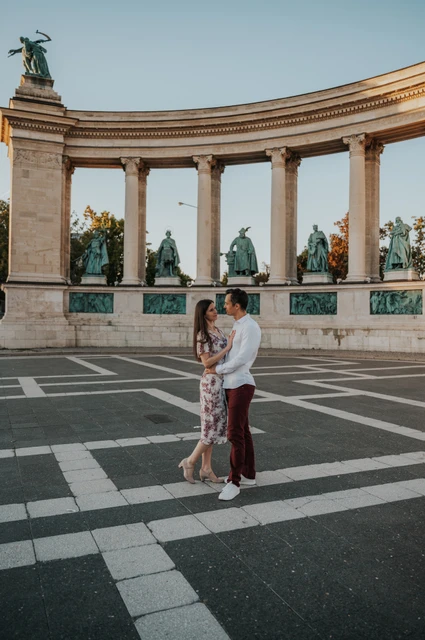An embrace beneath the colonnade at a Budapest couple photoshoot The couple embracing in a full-length portrait on the patterned paving at Heroes’ Square during their couple photoshoot in Budapest.