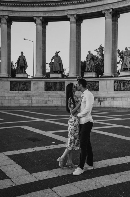 A kiss at Heroes’ Square in black and white at a Budapest couple photoshoot Black-and-white full-length portrait of the couple kissing on Heroes’ Square’s patterned paving during their couple photoshoot in Budapest.
