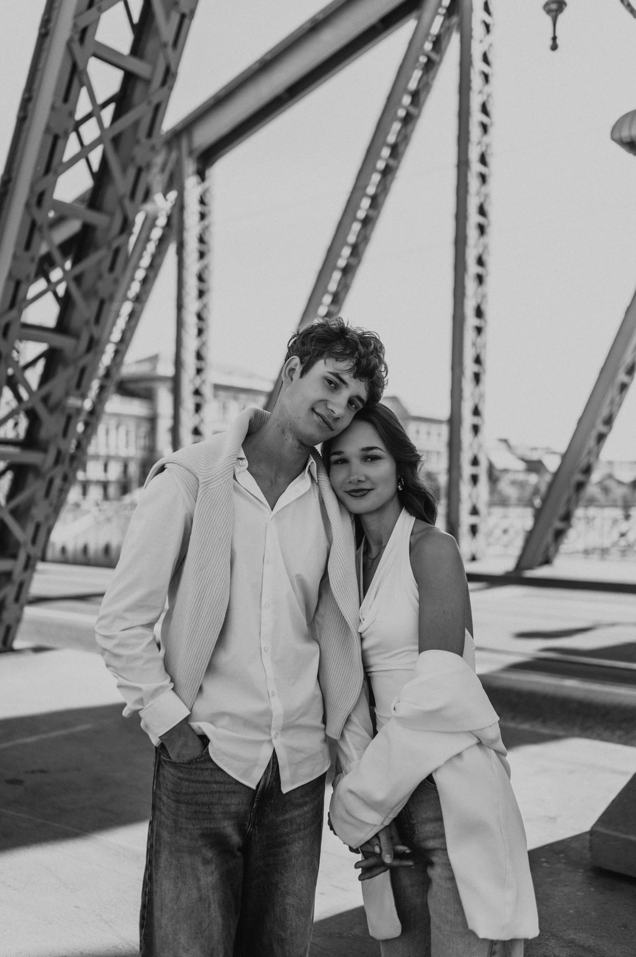 Black-and-white portrait of the couple leaning their heads together beneath the bridge beams during their Budapest photoshoot on Liberty Bridge.