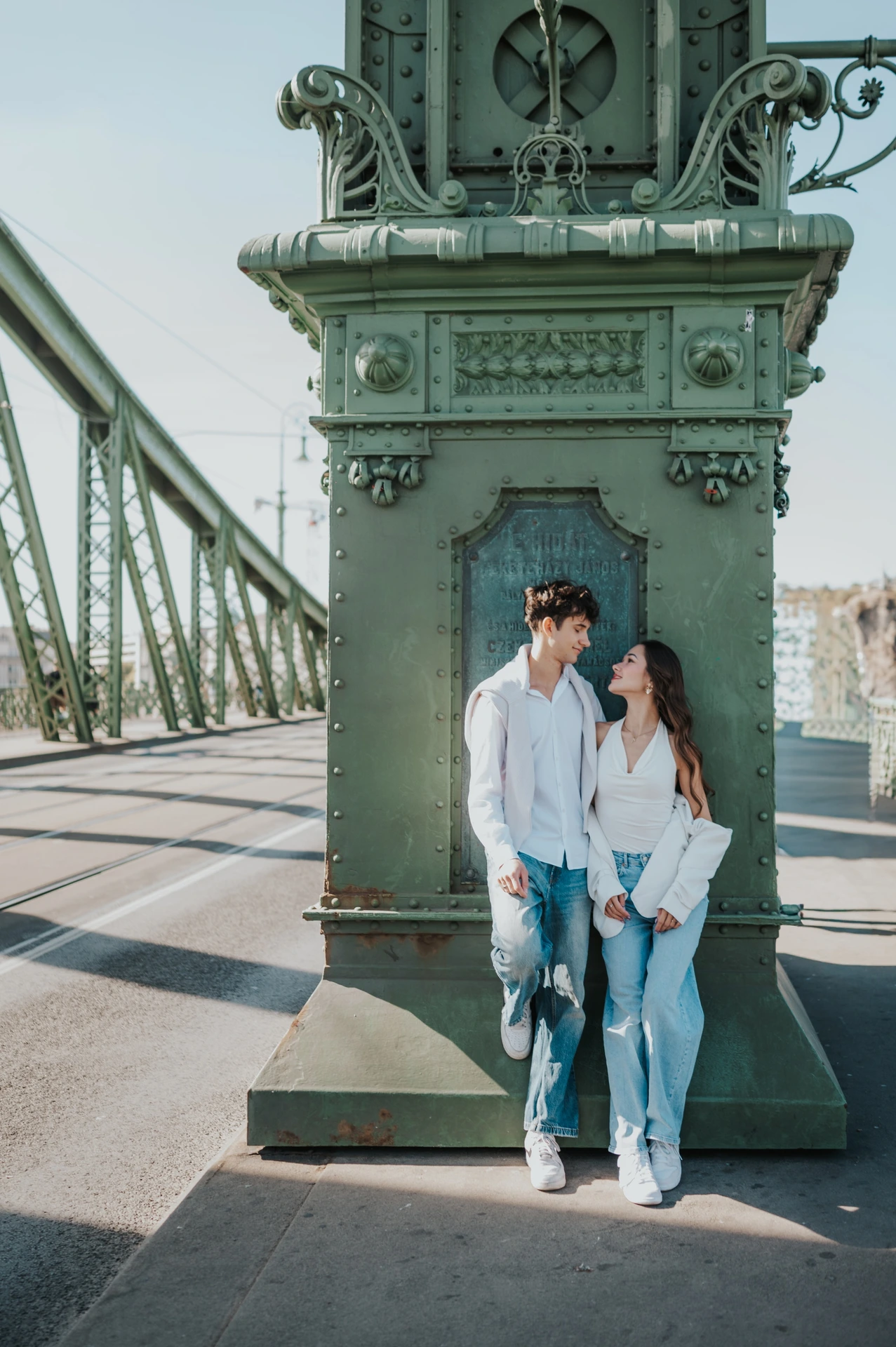 The couple standing together against an ornate green bridge pillar during their Budapest photoshoot on Liberty Bridge.
