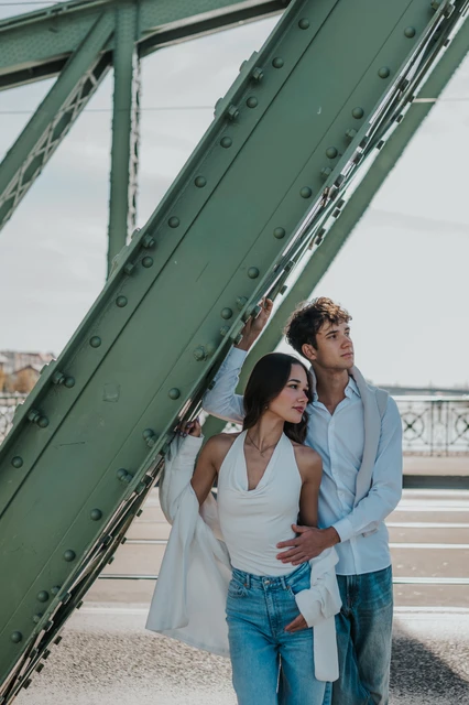 The couple looking away together while embracing beside a diagonal green beam during their Budapest photoshoot on Liberty Bridge.