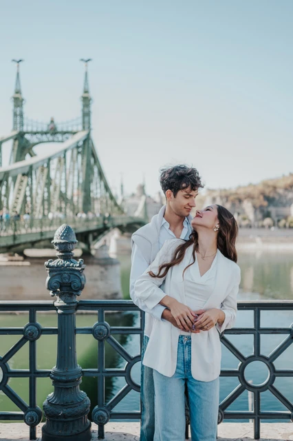 Photoshoot in Budapest embracing beside the river at Liberty Bridge The couple holding each other close beside the decorative riverside railing during their Budapest photoshoot near Liberty Bridge.