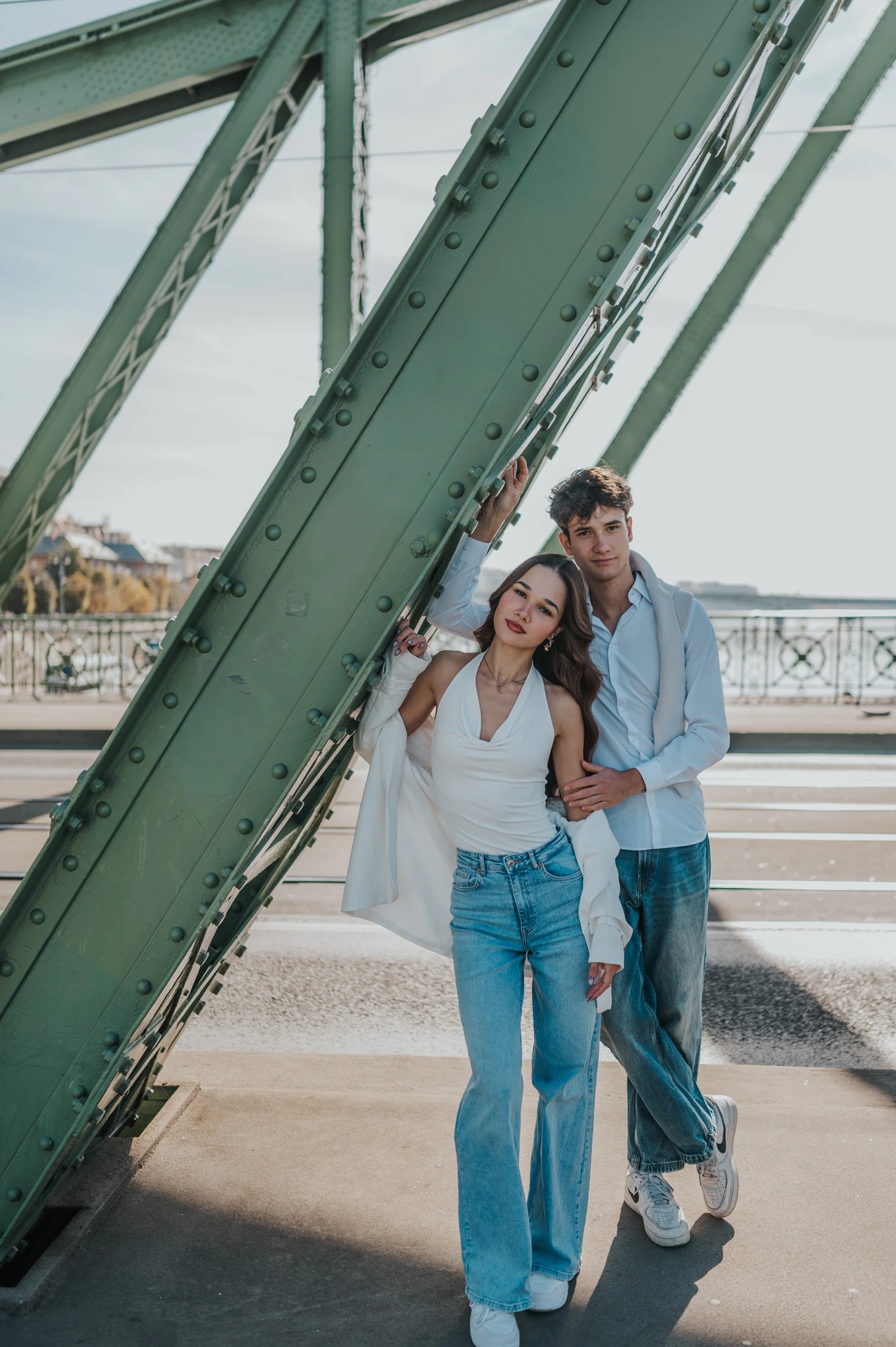 The couple standing close beneath the diagonal green steel beams during their Budapest photoshoot on Liberty Bridge.