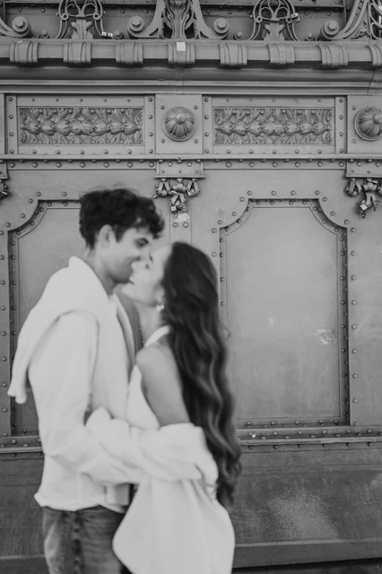 Budapest photoshoot kissing by the bridge pillar in black and white Black-and-white portrait of the couple kissing in front of the decorative bridge pillar during their Budapest photoshoot on Liberty Bridge.
