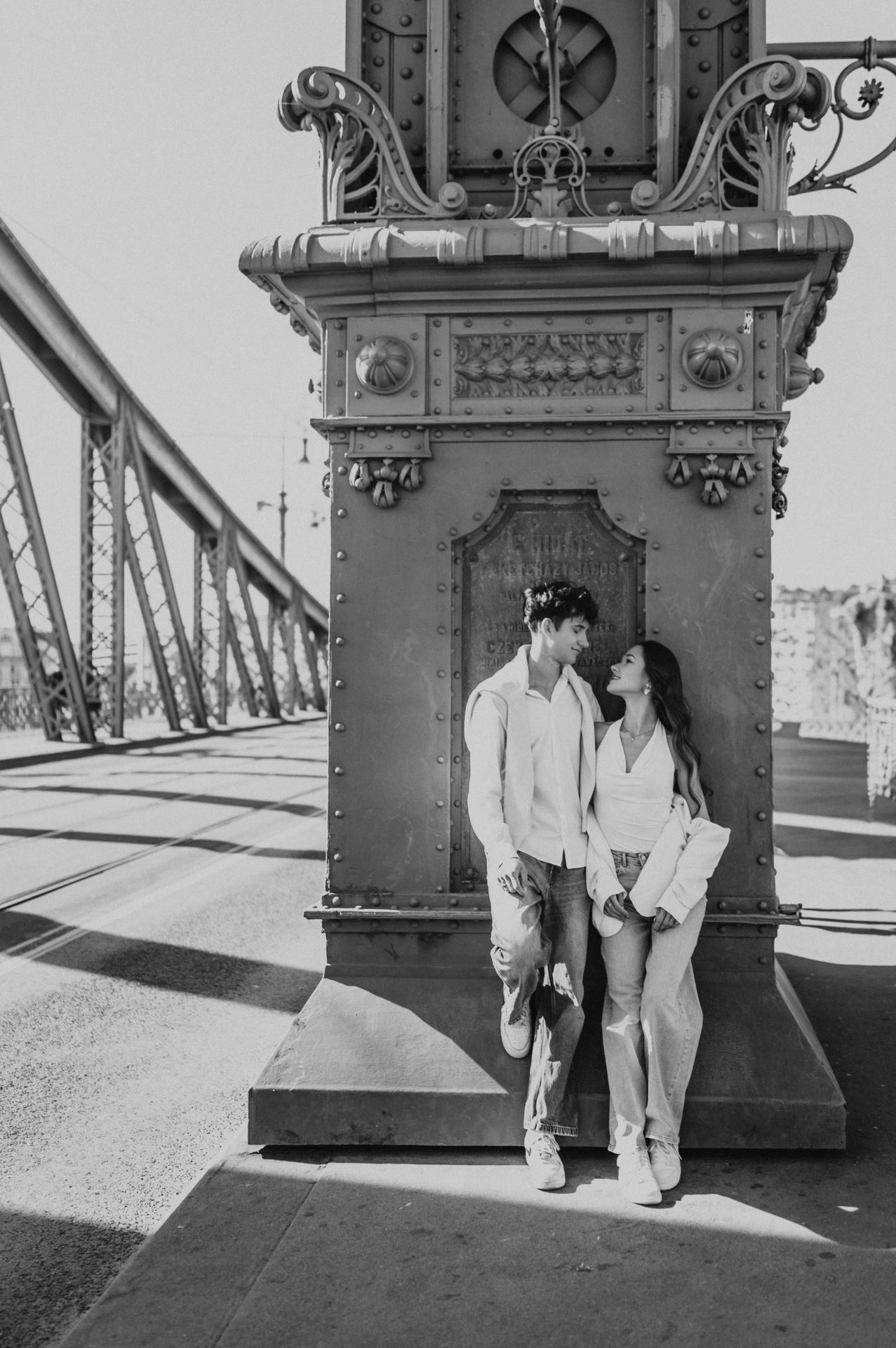 Black-and-white photograph of the couple standing against the ornate bridge pillar during their Budapest photoshoot on Liberty Bridge.