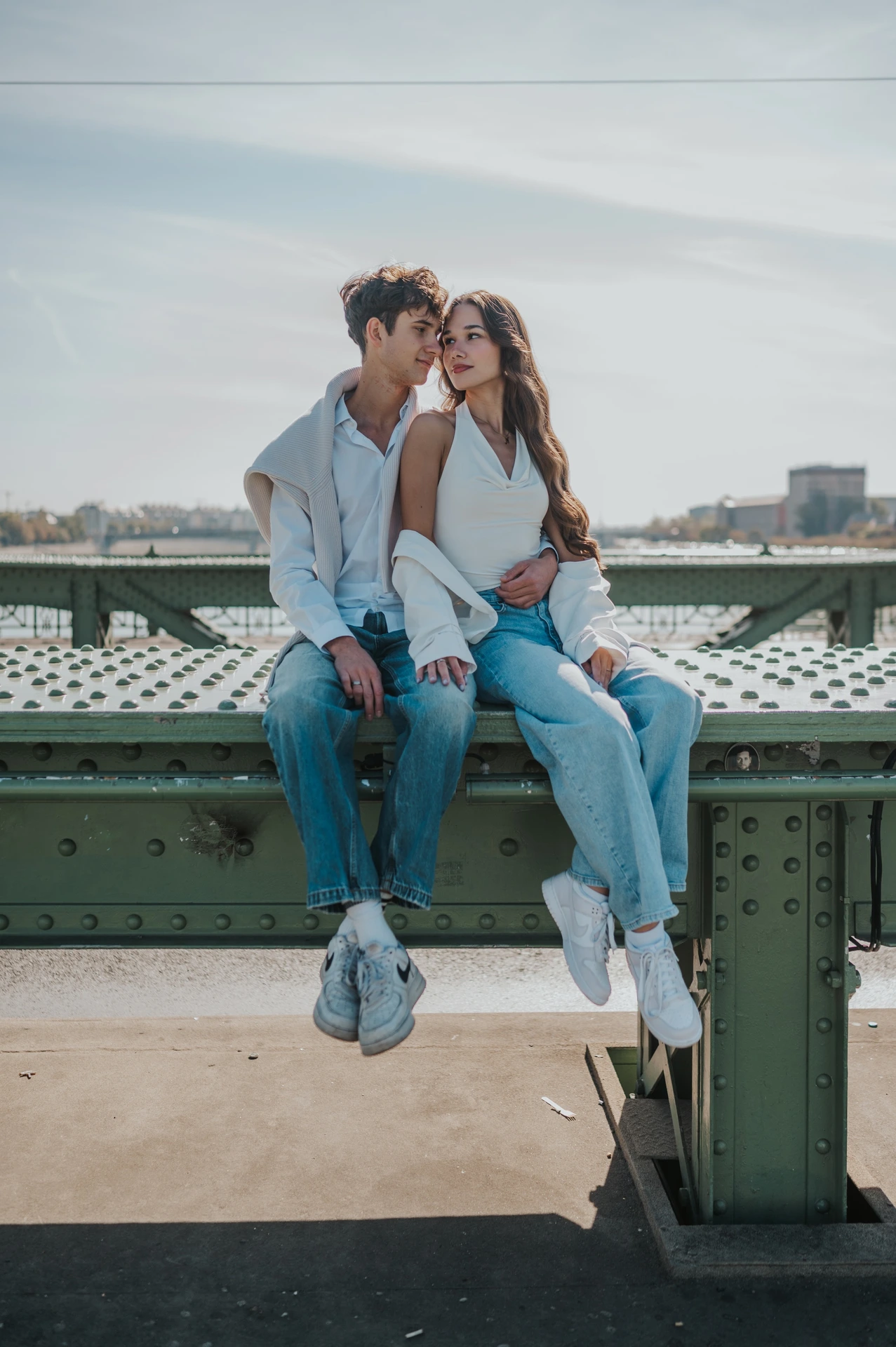 The couple sitting beside each other on the bridge railing and kissing during their Budapest photoshoot on Liberty Bridge.