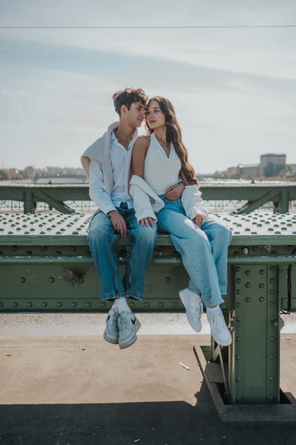 The couple sitting beside each other on the bridge railing and kissing during their Budapest photoshoot on Liberty Bridge.