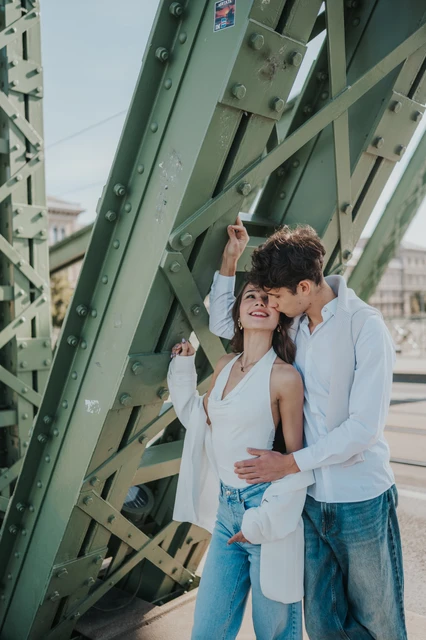Smiling couple photoshoot in Budapest beside the riveted bridge beams The couple smiling while standing close together beside the riveted green beams during their Budapest photoshoot on Liberty Bridge.