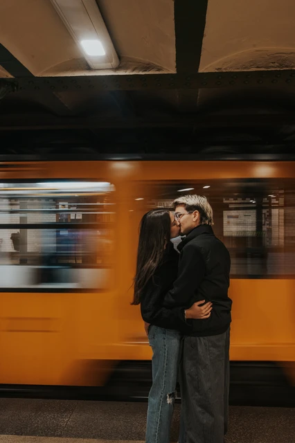 Budapest couple photoshoot with a passing yellow metro train The couple embracing on the platform during their Budapest photoshoot, with a yellow metro train blurred in motion behind them.