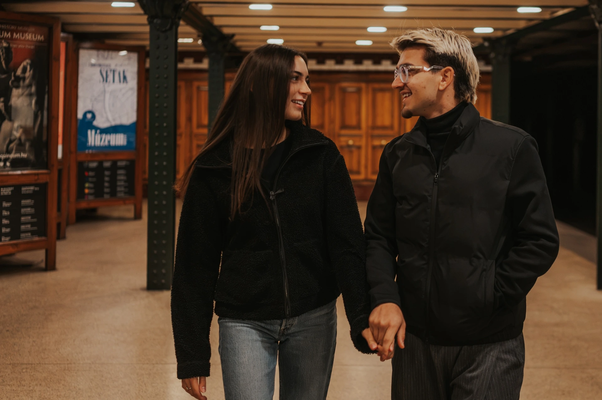 The couple smiling at each other and holding hands in the warmly lit metro station during their Budapest photoshoot.