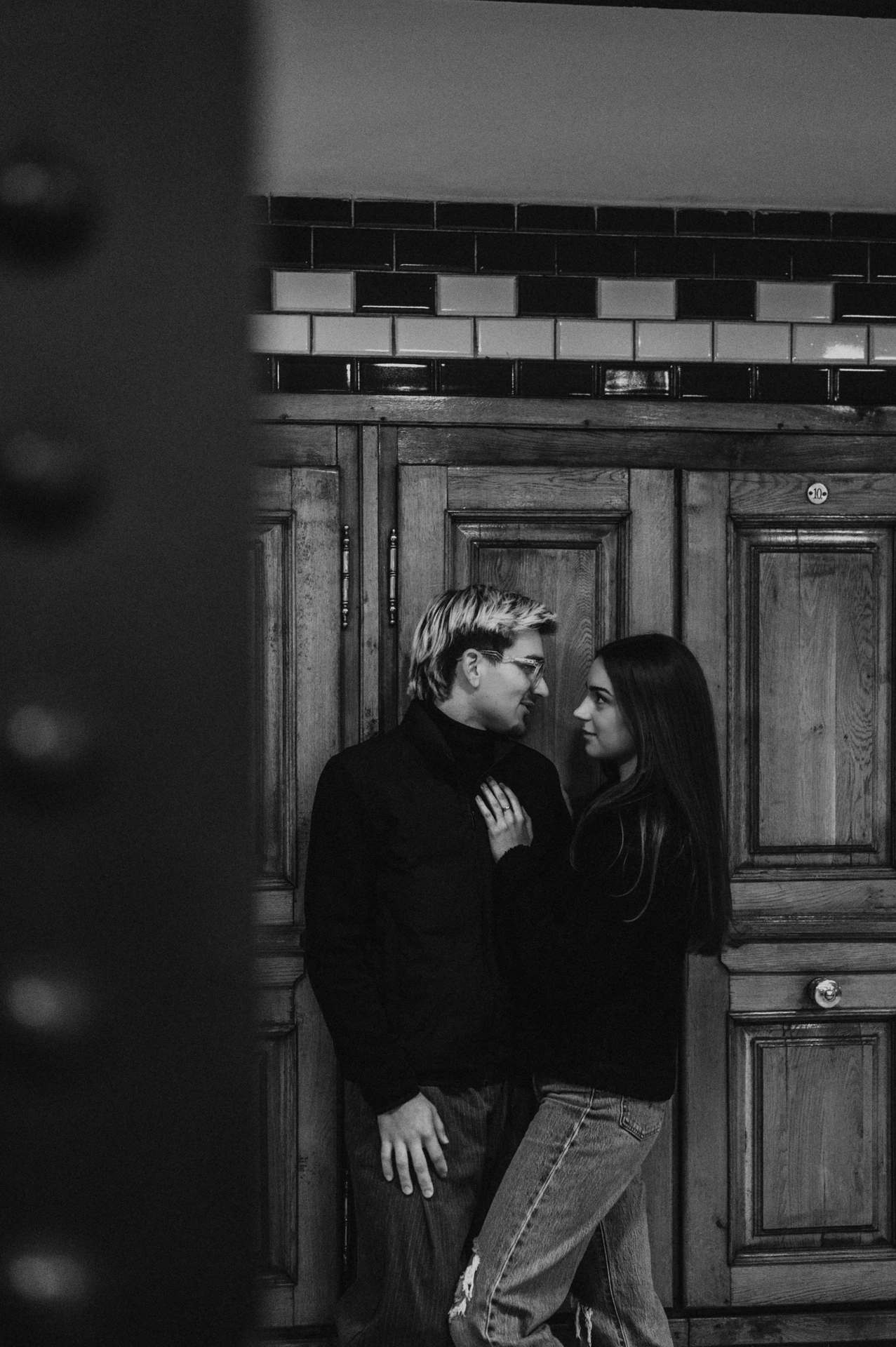 Black-and-white portrait of the couple leaning close beside the wooden station doors during their Budapest photoshoot.