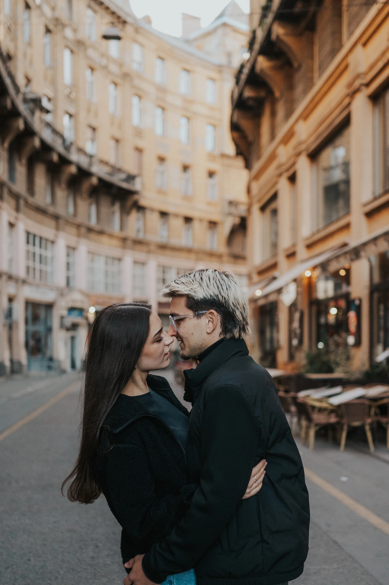 The couple kissing in the street during their Budapest photoshoot, with a curved building and rows of windows behind them.