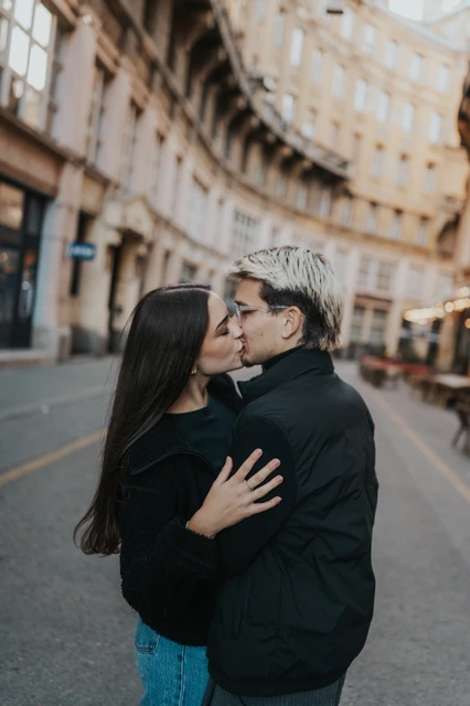 Close couple photoshoot in Budapest on a city street A close view of the couple kissing during their Budapest photoshoot on a city street, with the surrounding buildings softly blurred.