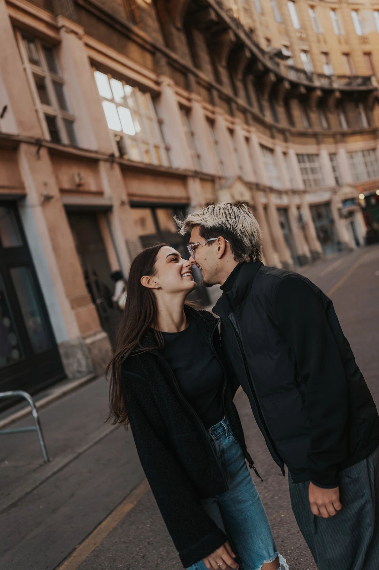A tilted portrait of the couple leaning towards each other for a kiss during their Budapest photoshoot beside the city buildings.