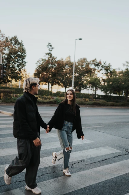 Budapest couple photoshoot crossing the city street together The couple crossing a city street together during their Budapest photoshoot, wearing dark jackets and casual trousers.