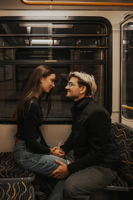 Budapest photoshoot seated together inside the metro carriage The couple seated close together inside the metro during their Budapest photoshoot, holding hands beside the window and patterned seats.