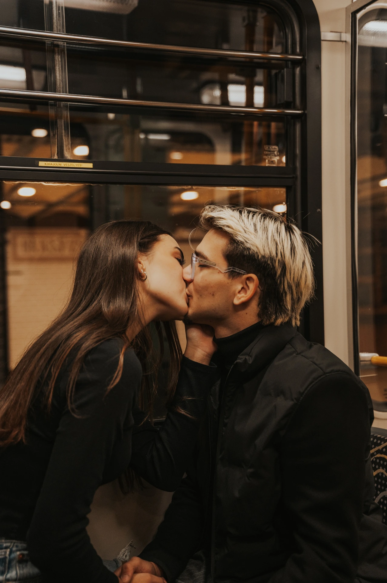 A close portrait of the couple kissing on the metro seats during their Budapest photoshoot, with the window behind them.
