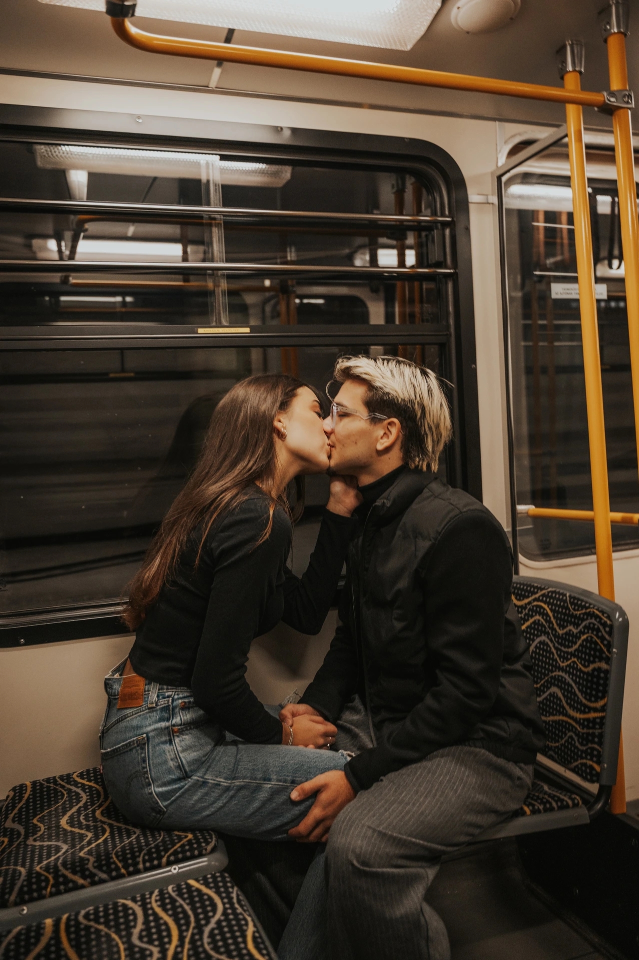 The couple leaning towards each other for a kiss on the patterned seats during their Budapest photoshoot inside the metro carriage.
