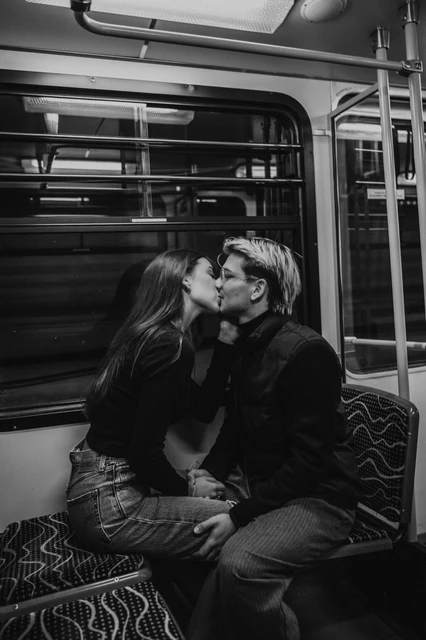 Budapest couple photoshoot on the metro seats in black and white Black-and-white photograph of the couple kissing on the metro seats during their Budapest photoshoot, framed by the carriage window.