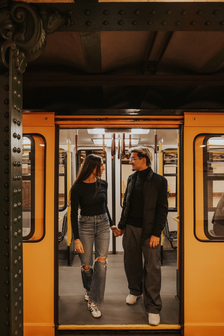 Budapest photoshoot framed by the open yellow metro doors The couple standing hand in hand inside a yellow metro carriage during their Budapest photoshoot, photographed through the open doors.