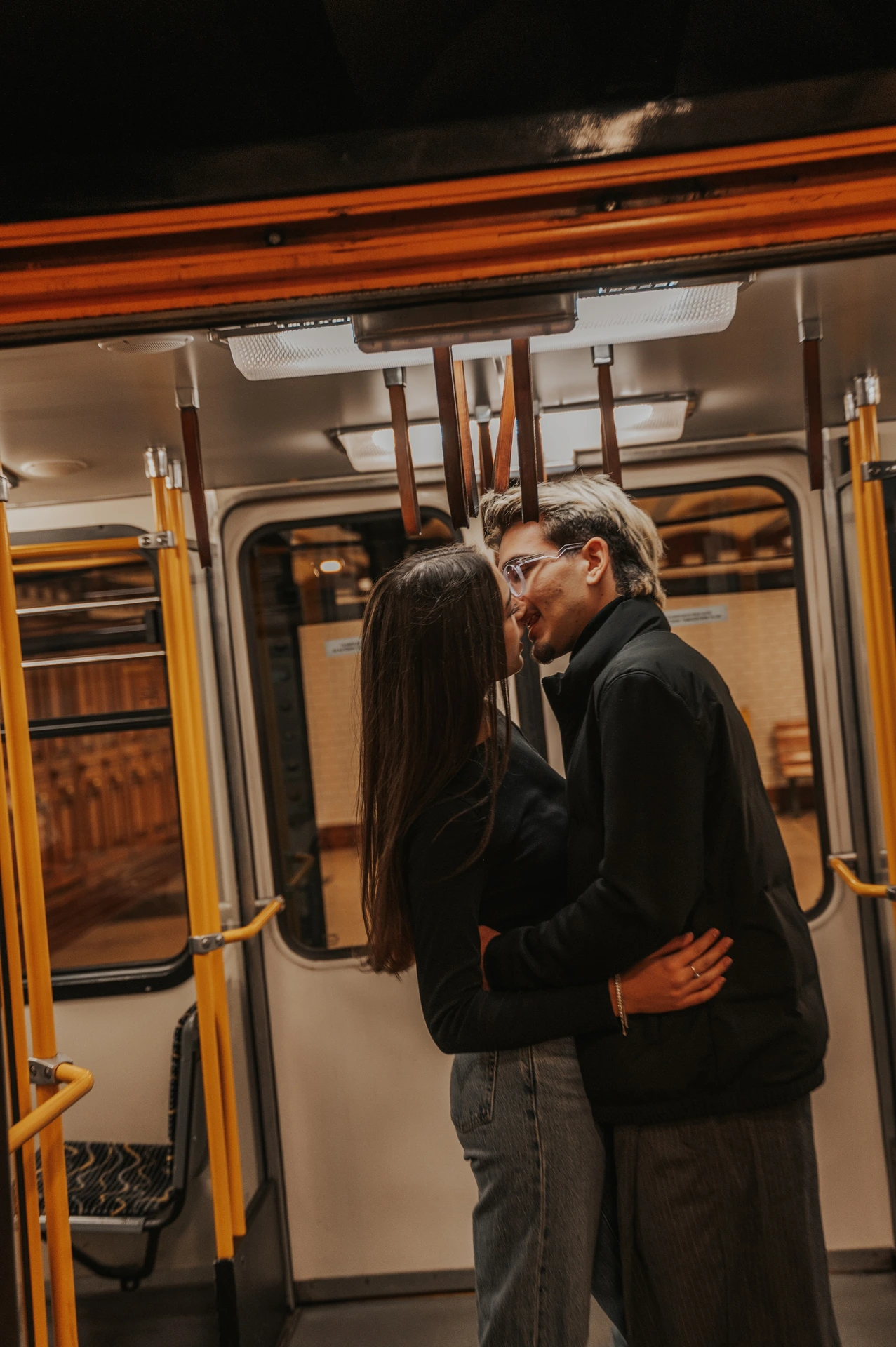 A tilted portrait of the couple embracing inside the metro carriage during their Budapest photoshoot, with yellow rails around them.