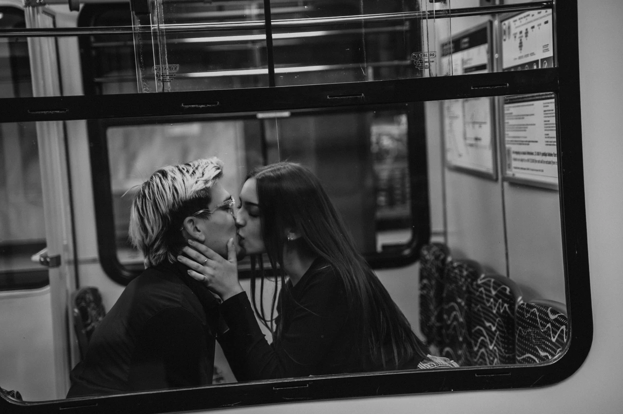 Budapest photoshoot through the metro window in black and white Black-and-white photograph of the couple kissing on the seats during their Budapest photoshoot, viewed through the metro carriage window.