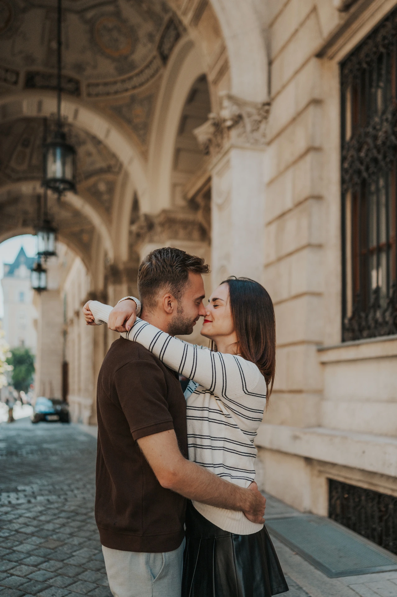 The couple leaning close beneath the Opera’s carved stone archway during a couple photoshoot in Budapest.