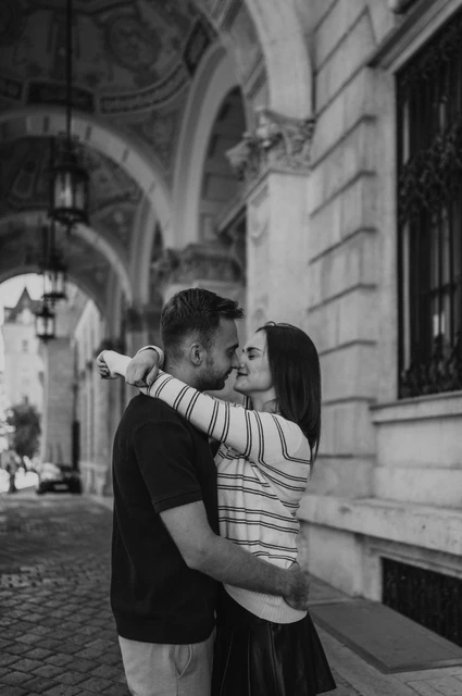Black-and-white photograph of the couple embracing beneath the Opera’s ornate stone arcade during a couple photoshoot in Budapest.