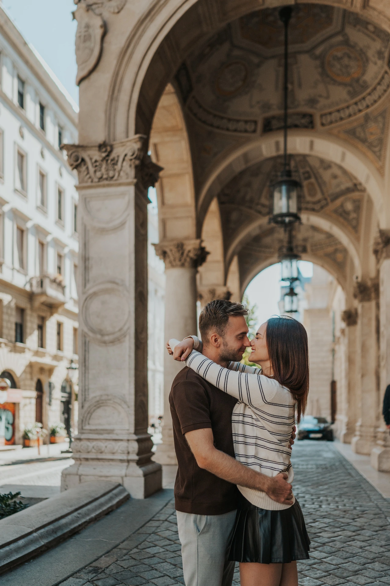 The couple embracing beneath the Opera’s carved stone arches and decorated ceiling during a couple photoshoot in Budapest.
