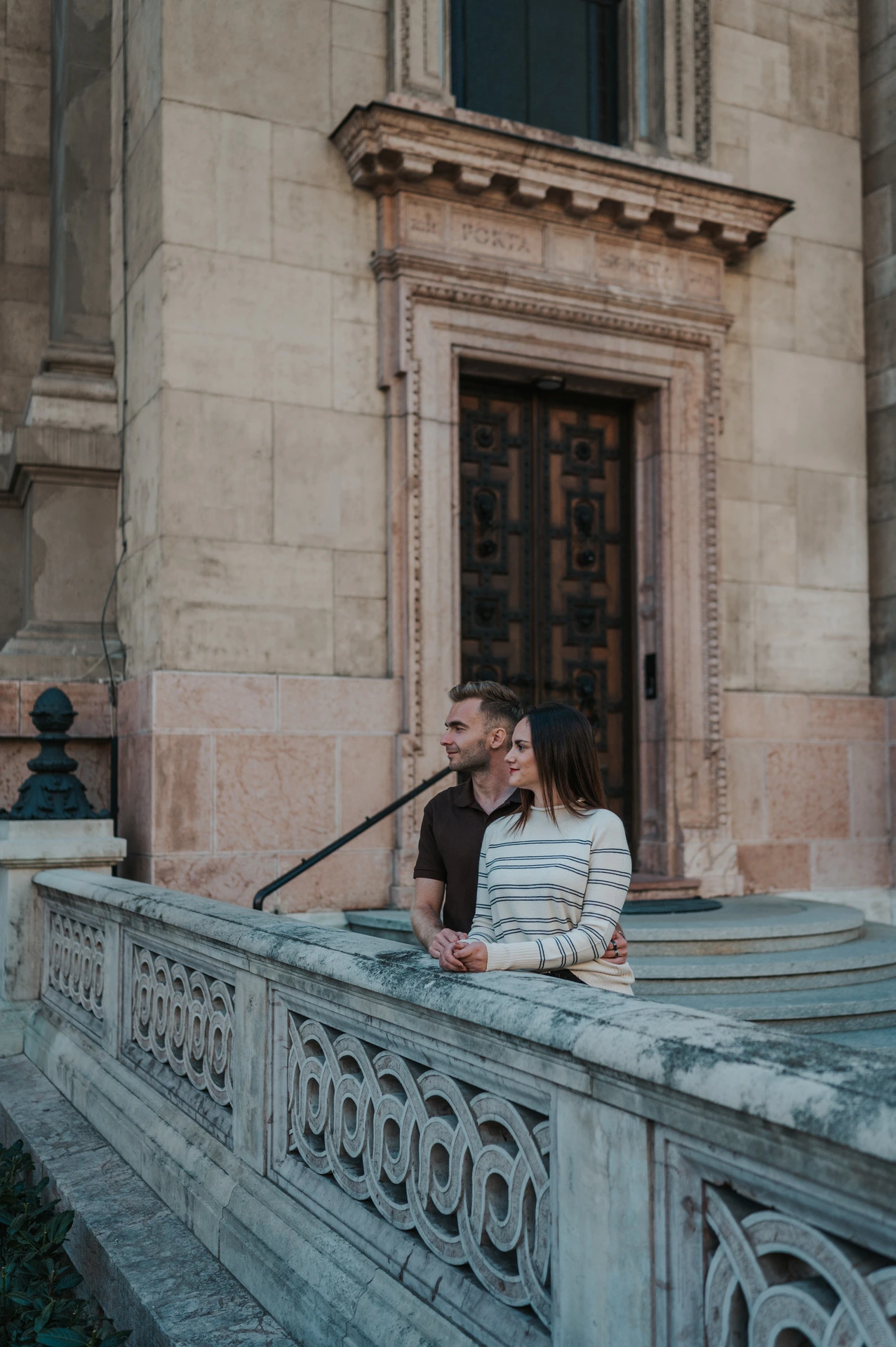 The man kissing his partner near her temple beside a stone balustrade at St Stephen’s Basilica during a couple photoshoot in Budapest.